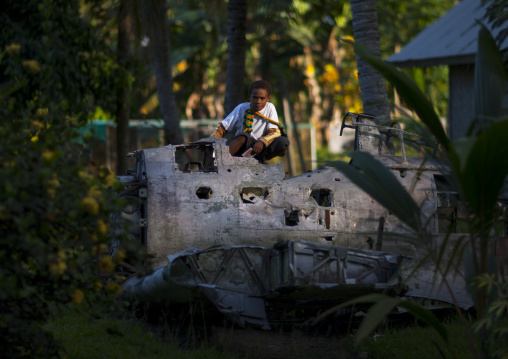 Boy sit on a plane wrecks in the war museum garden, East New Britain Province, Rabaul, Papua New Guinea