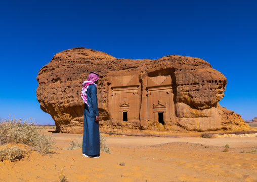 Saudi man walking in front of tombs in al-Hijr archaeological site in Madain Saleh, Al Madinah Province, Alula, Saudi Arabia
