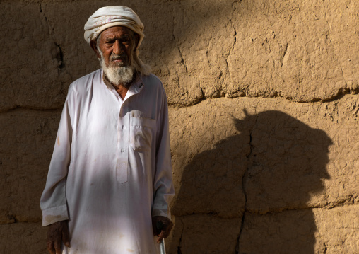 Old saudi man standing in front of a mud house, Najran Province, Najran, Saudi Arabia