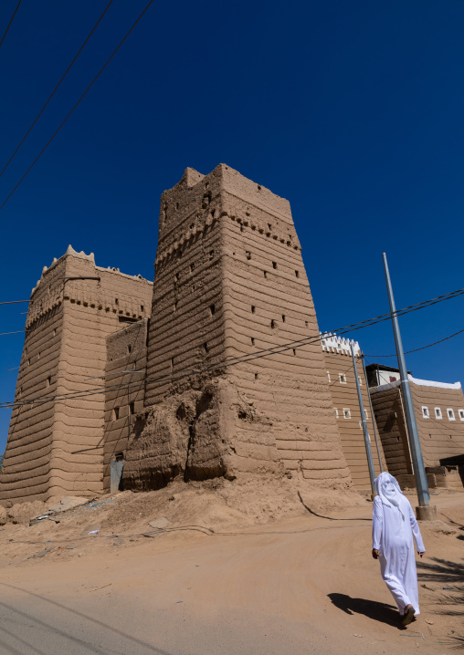 Saudi man passing in front of traditional old mud house, Najran Province, Najran, Saudi Arabia