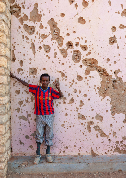 Somali boy with a barcelona football shirt in front of a wal full of bullets holes, Togdheer region, Burao, Somaliland