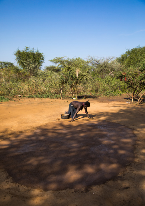 Larim tribe woman making a clean courtyard in front of her hut, Boya Mountains, Imatong, South Sudan