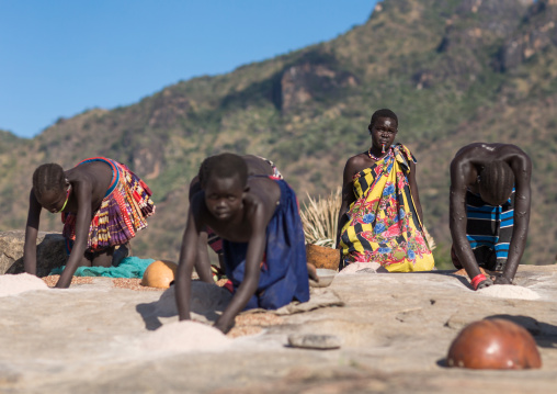 Larim tribe women grinding sorghum grains in holes in a rock, Boya Mountains, Imatong, South Sudan