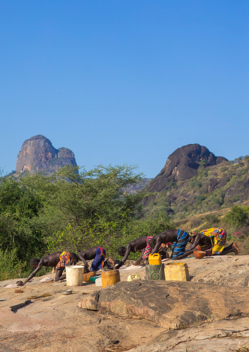 Larim tribe women grinding sorghum grains in holes in a rock, Boya Mountains, Imatong, South Sudan