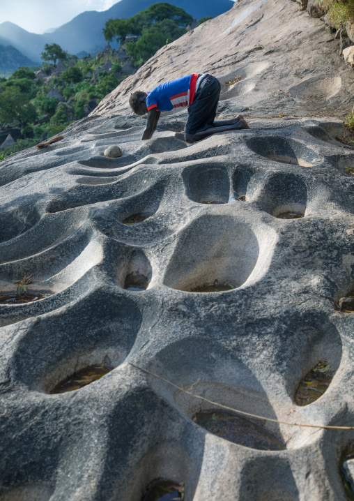 Lotuko tribe woman grinding grains in a hole in the rock, Central Equatoria, Illeu, South Sudan