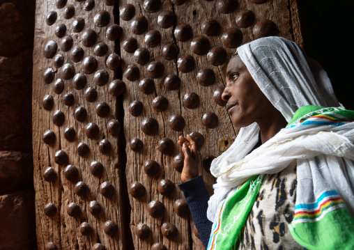 Ethiopian woman pilgrim in front of an old wooden door, Amhara Region, Lalibela, Ethiopia