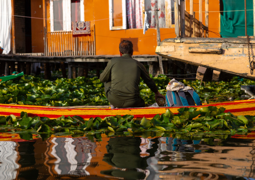 Man on a boat passing in front of a houseboat on Dal Lake, Jammu and Kashmir, Srinagar, India