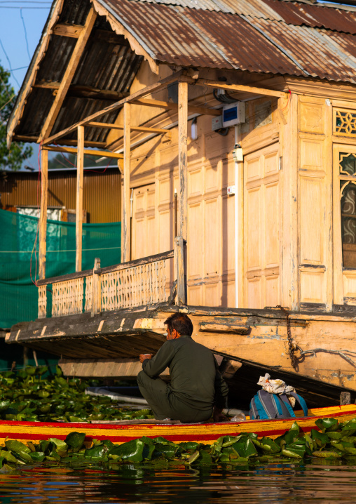 Man on a boat passing in front of a houseboat on Dal Lake, Jammu and Kashmir, Srinagar, India