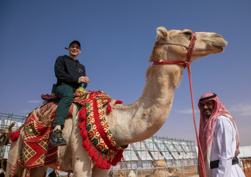 Tourist riding a camel during King Abdul Aziz Camel Festival, Riyadh Province, Rimah, Saudi Arabia