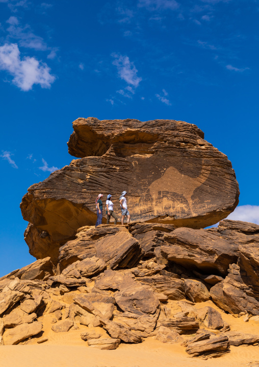 Tourists in front of Jabal Al-Mawaqi giant camel rock art, Najran Province, Thar, Saudi Arabia