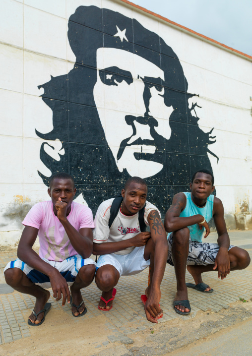 Three angolan men squatting in front of a wall painting of Che Guevara, Luanda Province, Sumbe, Angola