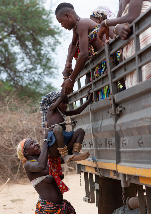 Mucubal tribe people jumping on the back of a truck, Namibe Province, Virei, Angola