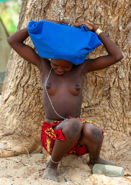 Mucubal tribe young woman ajusting a blue headwear, Namibe Province, Virei, Angola