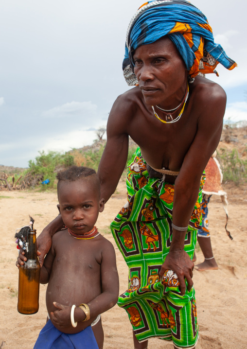 Mucubal tribe woman with her child who plays with a doll made of a beer bottle, Namibe Province, Virei, Angola