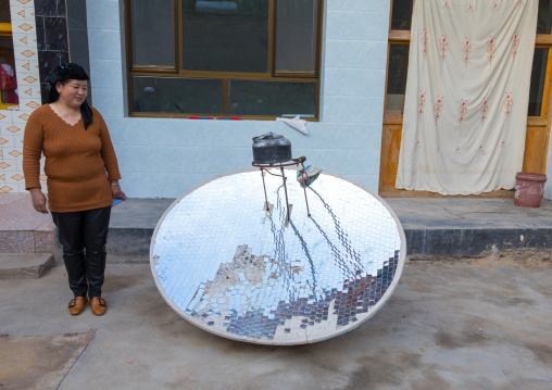Salar ethnic minority woman in front of a solar energy cookery used to boil water, Qinghai province, Xunhua, China