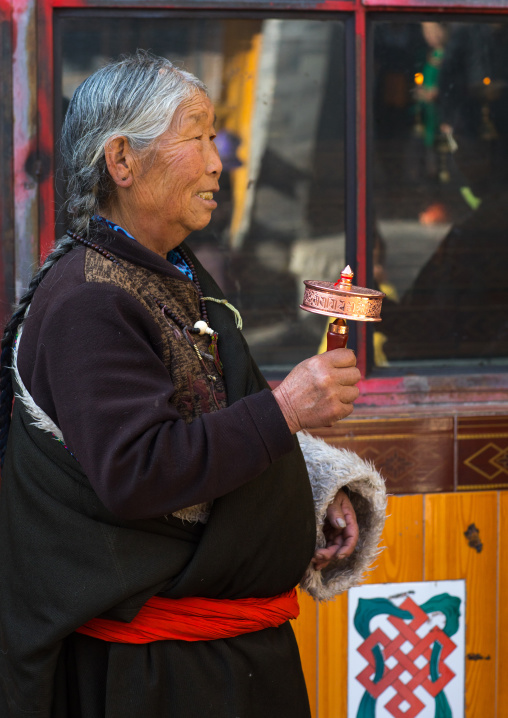 Tibetan pilgrim woman with a hand prayer wheel in Rongwo monastery, Tongren County, Longwu, China