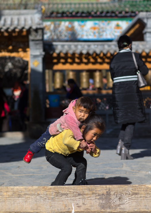 Tibetan girl carrying her brother on her back in Rongwo monastery, Tongren County, Longwu, China