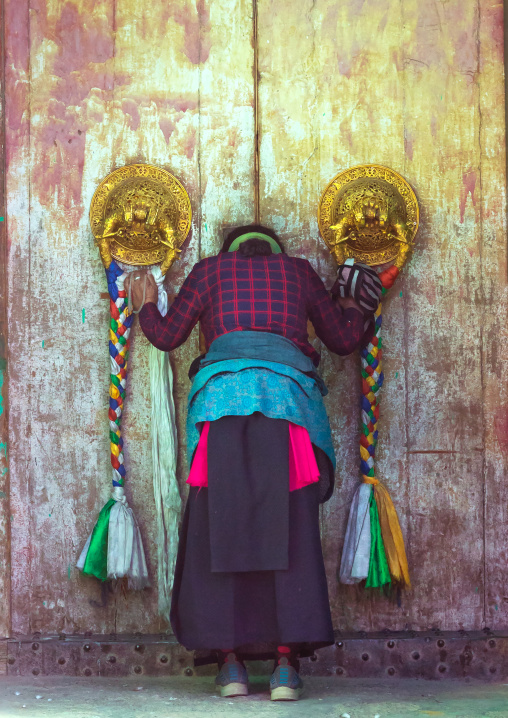Tibetan woman praying in front of a traditional door in Rongwo monastery, Tongren County, Longwu, China