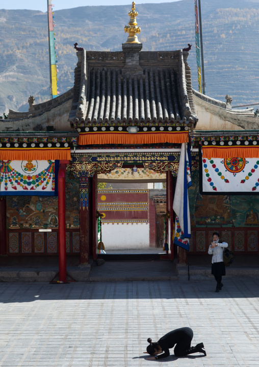Tibetan woman praying in the middle of the temple courtyard in Rongwo monastery, Tongren County, Longwu, China