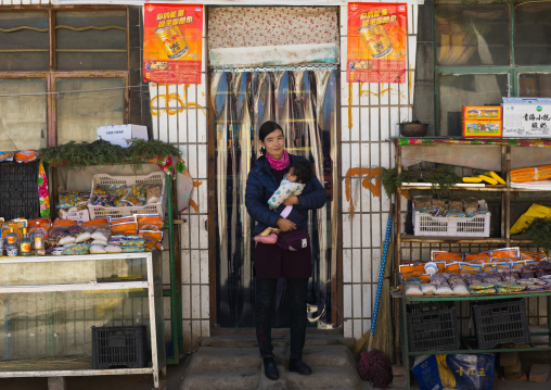 Tibetan woman with her baby in front of a shop, Tongren County, Longwu, China