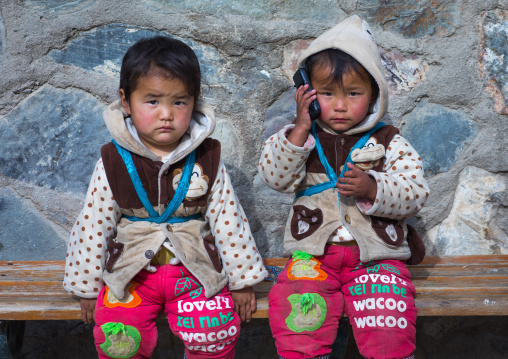 tibetan Children sit on a bench and playing with a mobile phone, Gansu province, Labrang, China