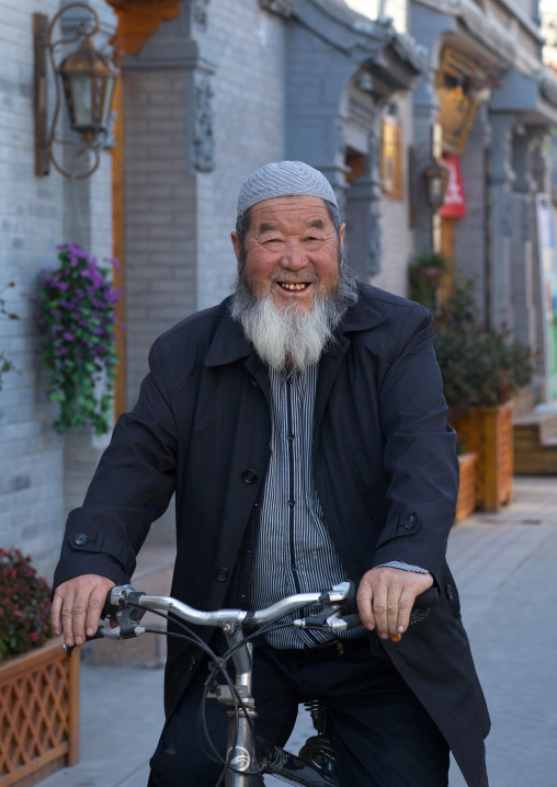 Smiling hui muslim man riding a bicycle in the street, Gansu province, Linxia, China