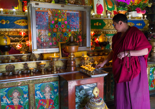 tibetan Monk lightening butter lamps inside Rongwo monastery, Tongren County, Longwu, China