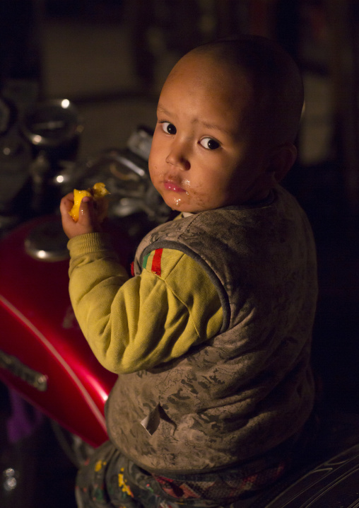 Uyghur Baby Eating A Fruit At Night Market, Hotan, Xinjiang Uyghur Autonomous Region, China