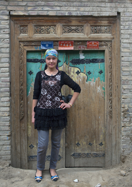 Young Uyghur Woman Posing In Front Of A Traditional Door In Old Town, Keriya, Xinjiang Uyghur Autonomous Region, China