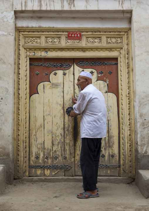 Old Uyghur Man In Front Of A Traditional Door In Old Town, Keriya, Xinjiang Uyghur Autonomous Region, China