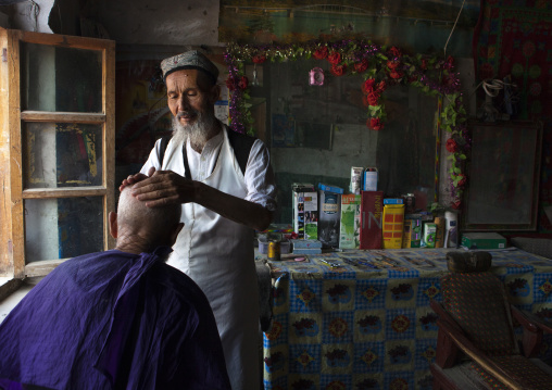 Uyghur Barber In His Shop Shaving The Head Of A Client, Minfeng, Xinjiang Uyghur Autonomous Region, China