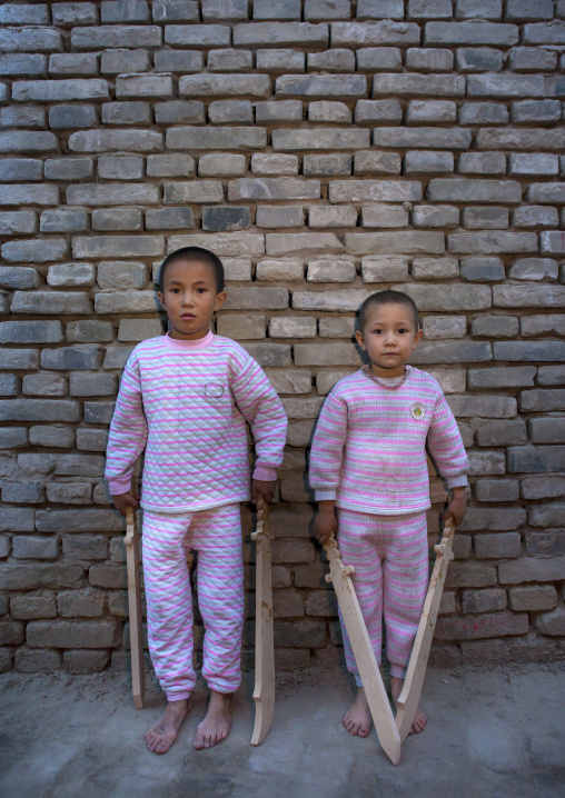 Uyghur Kids With Wooden Swords In The Street Posing Against A Brick Wall, Yarkand, Xinjiang Uyghur Autonomous Region, China