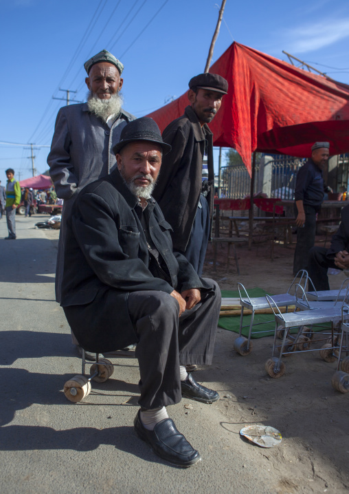 Uyghur Man Sitting On A Chair With Wheels Used To Harvest Cotton, Serik Buya Market, Yarkand, Xinjiang Uyghur Autonomous Region, China