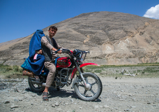 Afghan man riding a motorcycle with his wife wearing a burka, Badakhshan province, Qazi deh, Afghanistan