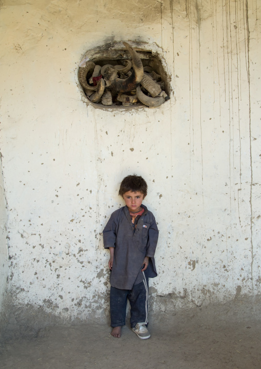 Afghan boy standing below ibex horns used during ramadan and nowruz celebrations, Badakhshan province, Zebak, Afghanistan