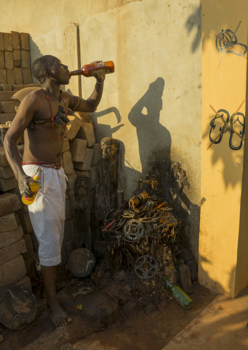 Benin, West Africa, Bonhicon, kagbanon bebe voodoo priest drinking orange juice and spitting it on ogun god altar made with pedaliers biking