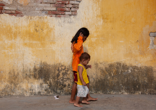 Two children holding hands and walking along a wall, Battambang province, Battambang, Cambodia