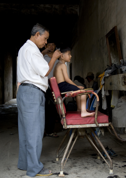 A boy having his hair cut by a man in a salon, Phnom Penh province, Phnom Penh, Cambodia