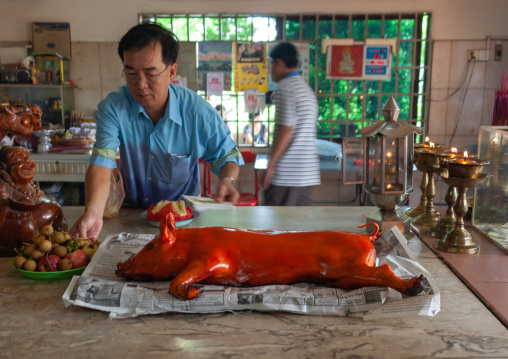 Cambodian man making offering with a roasted pig in a temple, Phnom Penh province, Phnom Penh, Cambodia