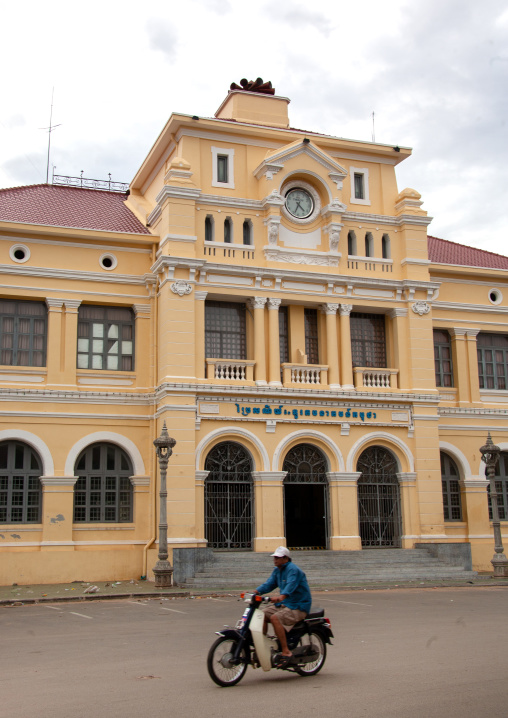 Cambodian man on a motorbike passing in front of the french-era post office, Phnom Penh province, Phnom Penh, Cambodia
