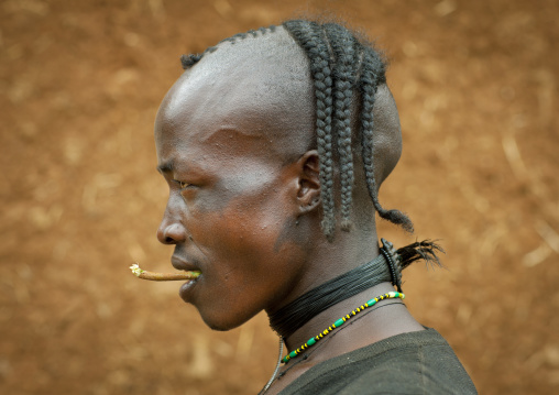 Portait of a fashionable tsemay tribe man with a traditional hairstyle posing in key afer, Omo valley, Ethiopia