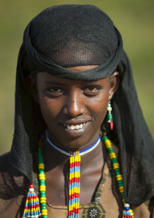 Portrait Of A Young Oromo Tribe Woman With Toothy Smile, Colourful Jewels And Black Headscarf, Harar, Ethiopia