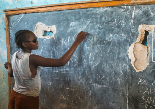 A nyangatom tribe teenage girl with sunglasses writes on a chalkboard, Omo valley, Kangate, Ethiopia