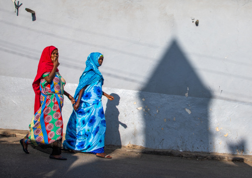 Ethiopian women passing in front of the shadow of a mosque minaret in the street, Harari region, Harar, Ethiopia