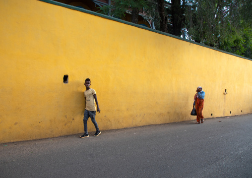Ethiopian people passing along a yellow wall in the old city, Harari region, Harar, Ethiopia