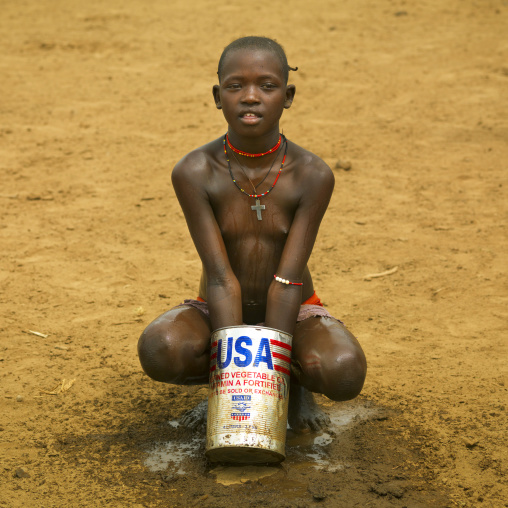 Young tsemay tribe girl washing herself with usa aid can, Omo valley, Ethiopia