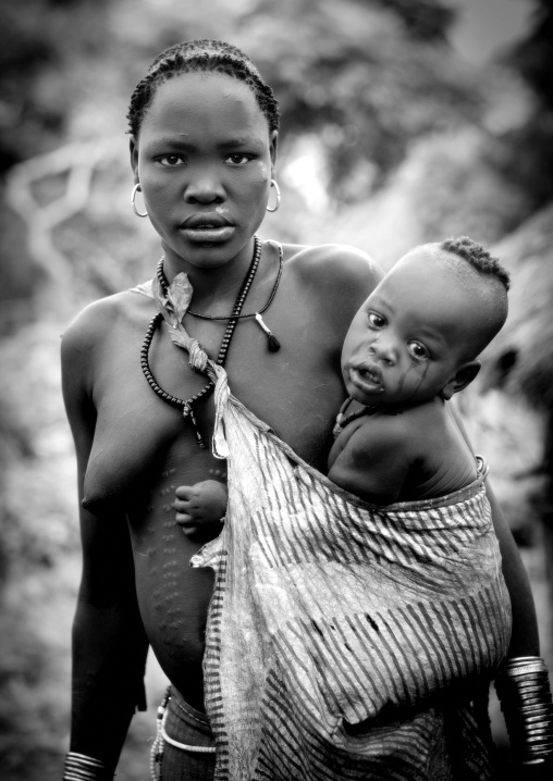 Black And White Portrait Of A Bodi Tribe Mother Carrying Her Baby, Hana Mursi, Omo Valley, Ethiopia