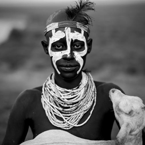 Black And White Portrait Of A Karo Tribe Man With Painted Face Holding A Goat In His Arms, Korcho Village, Omo Valley, Ethiopia