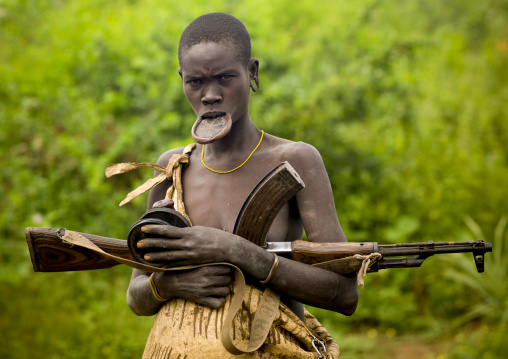 Mursi Tribe Woman With A Lip Plate, A  Kalashnikov Rifle And Two Clay Plates In Her Hands, Omo Valley, Ethiopia