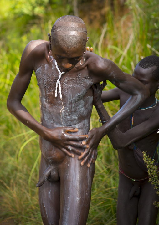 Man from Suri tribe receiving help to decorate his body with paintings, Tulgit, Omo valley, Ethiopia